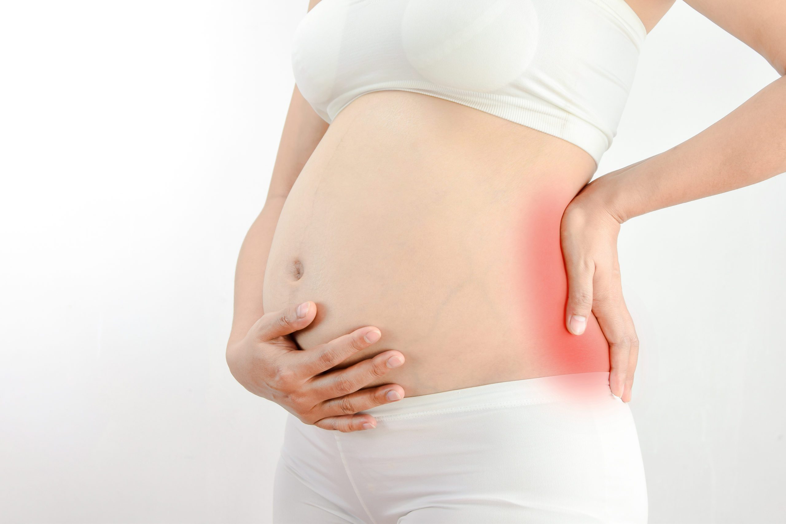 A woman in white underwear and a white top is holding her lower back and hip, which are highlighted in red, indicating pain. She appears to be seeking back pain relief. The background is plain and white.